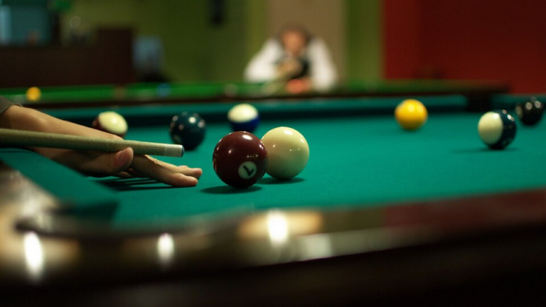 Une main s'apprête à jouer un coup de billard avec quelques billes sur le tapis